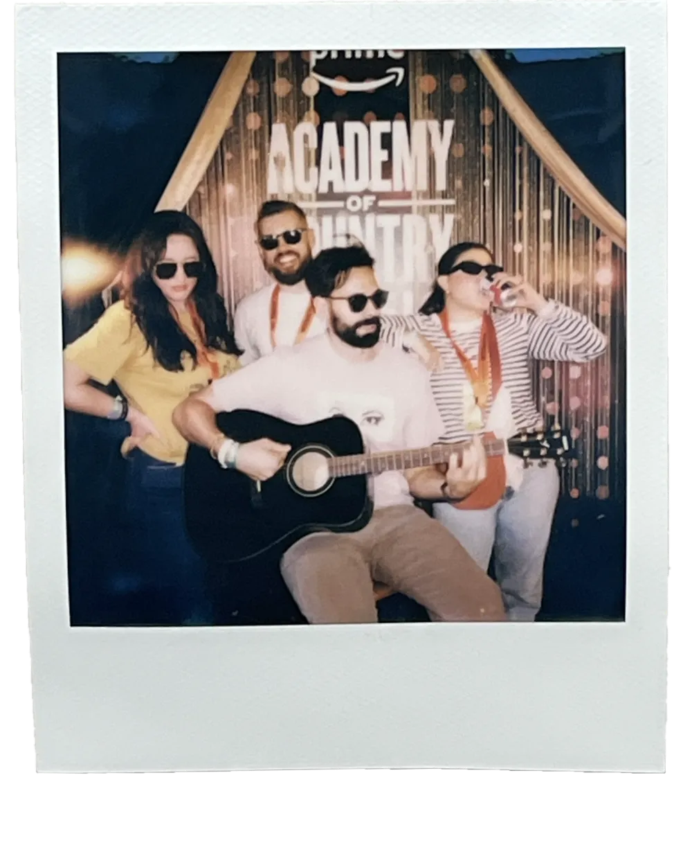 Polaroid of Nic playing acoustic guitar with friends in sunglasses at an Academy of Country Music photo booth